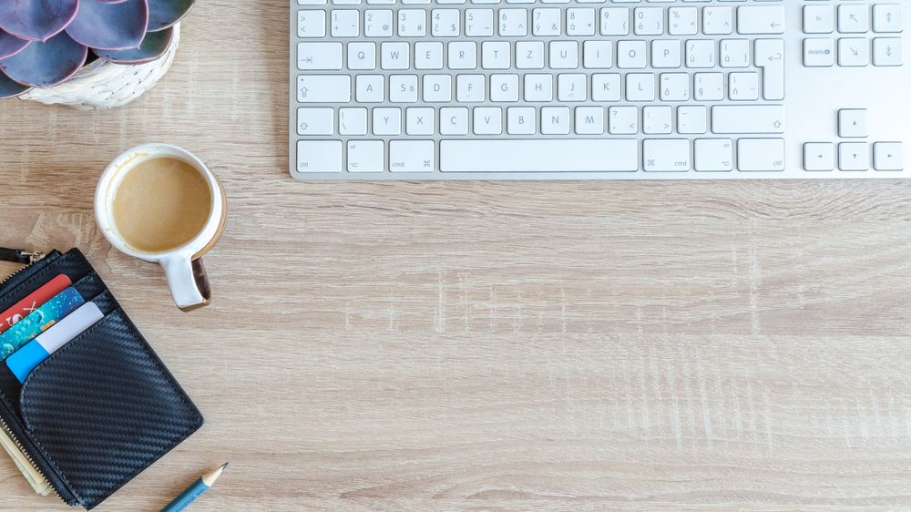 An organized workspace with a keyboard, coffee cup, wallet, and succulent plant on a wooden desk.