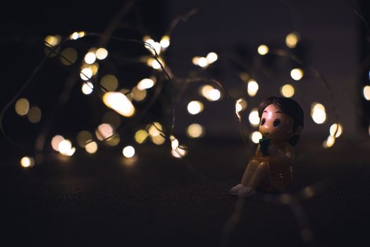 A whimsical close-up of a small figurine surrounded by enchanting fairy lights in a dark setting.