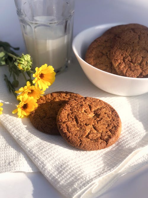 Brown Cookies Beside Bunch of Beautiful Yellow Flowers and a Glass of Milk