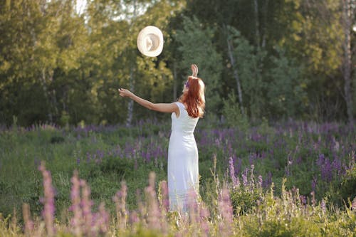 Woman in White Dress Throwing Her Sun Hat while Standing on a Lavender Field