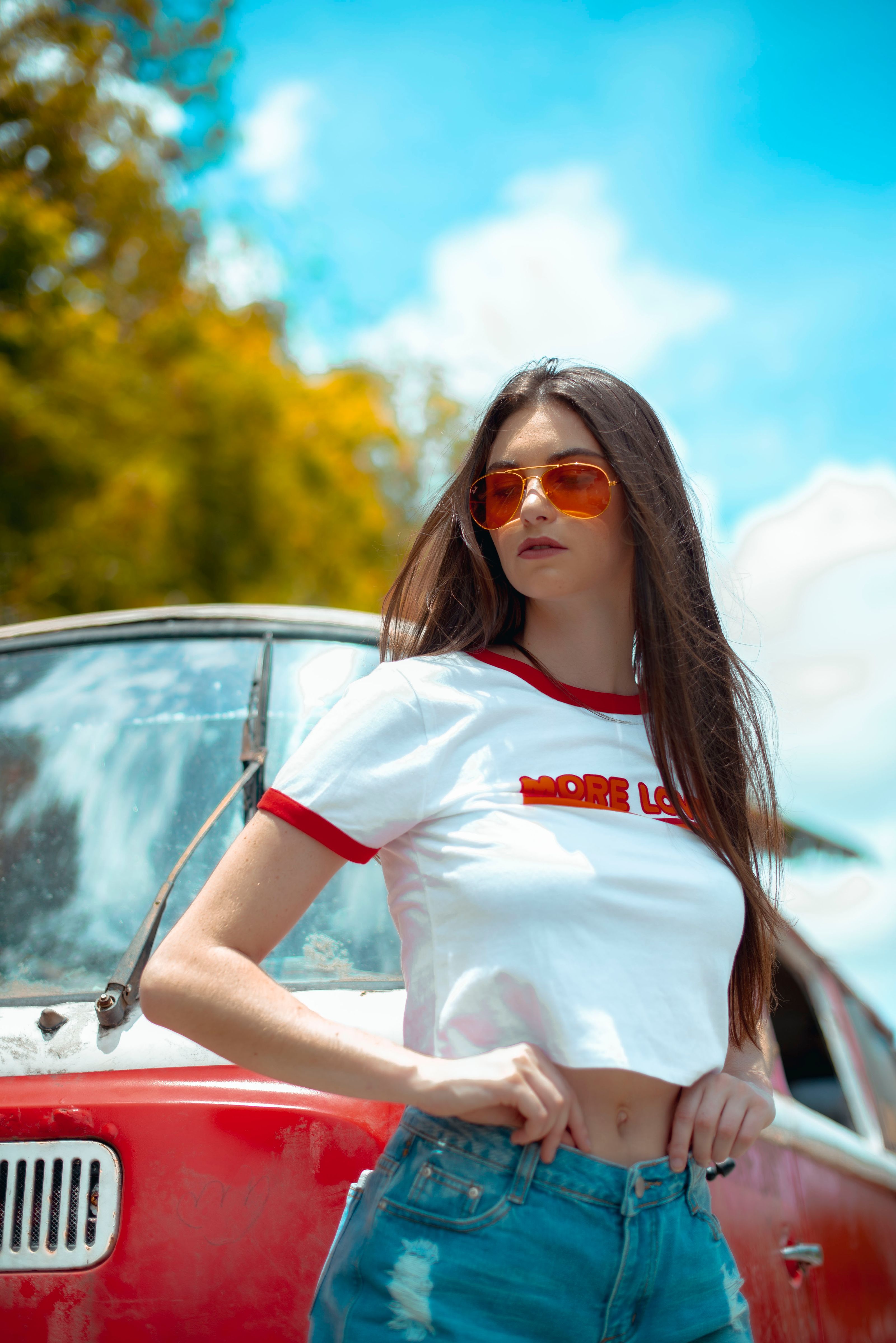 Mulher estilosa de óculos escuros e top cropped posando confiante ao lado de um carro clássico.