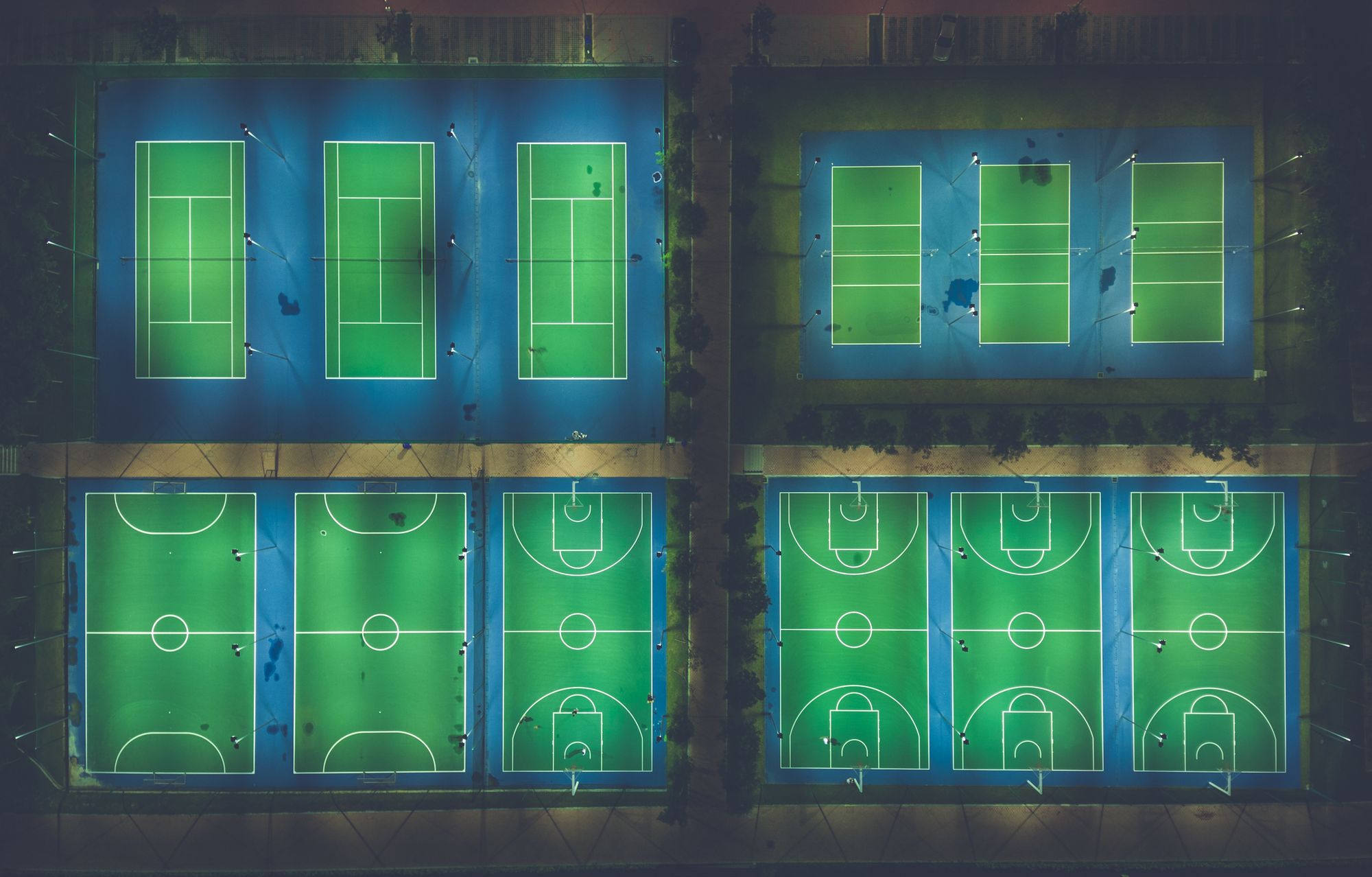 Cancha de tenis de superficie dura iluminada de noche, vista desde las gradas vacías