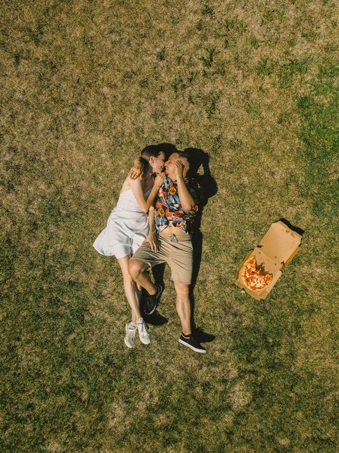 Couple lying on grass with pizza box, enjoying a sunny day outdoors.