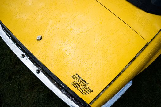 Close-up of a Triumph Spitfire 1500 yellow hood with raindrops, viewed from above.