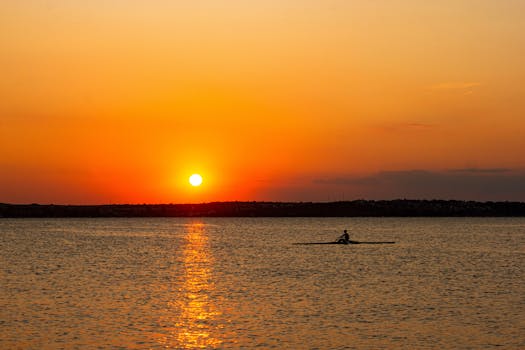 Captivating silhouette of a lone boatman rowing during a vibrant sunset on a tranquil lake.