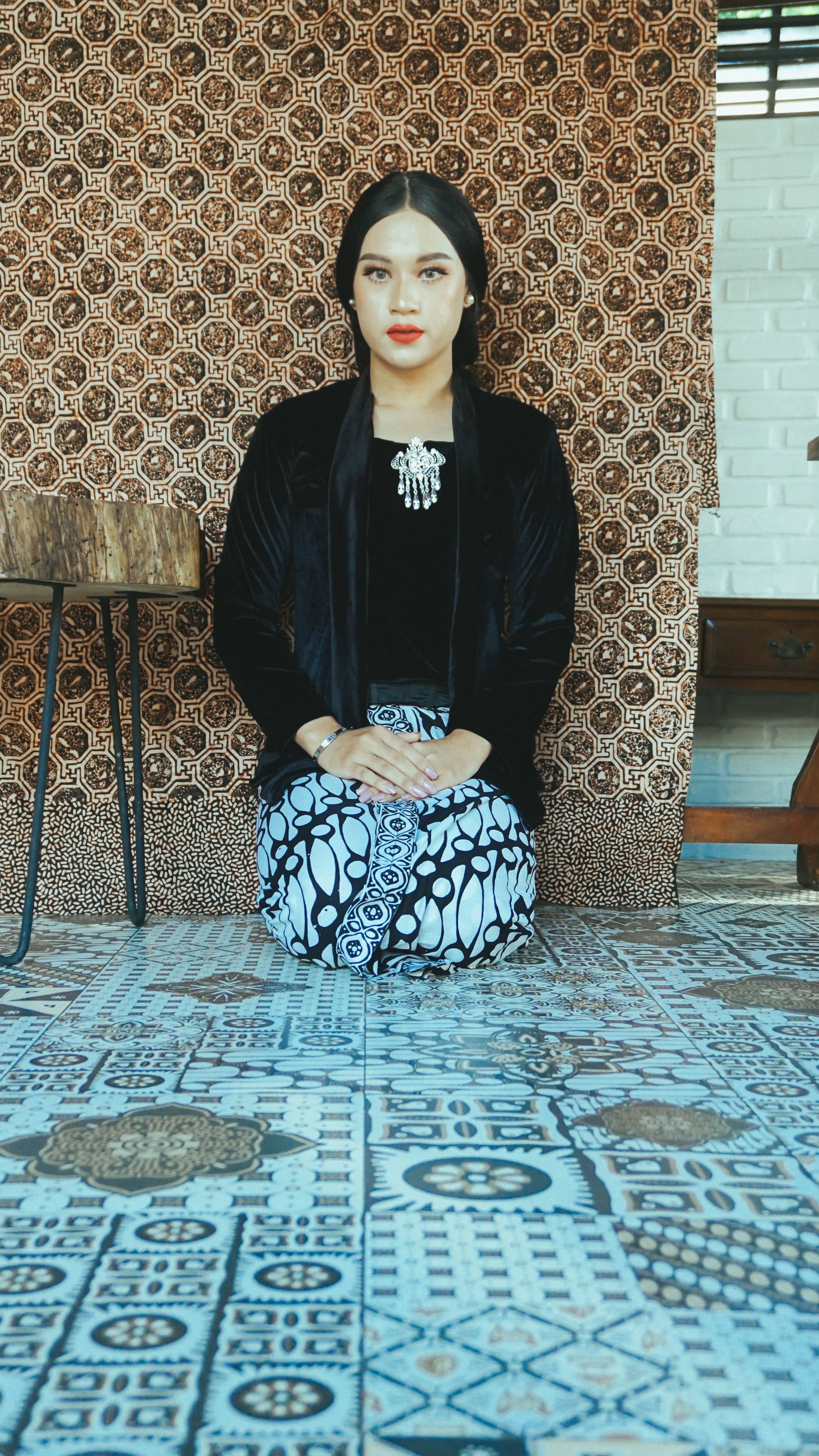Elegant woman kneeling in traditional clothing, displaying cultural fashion indoors.