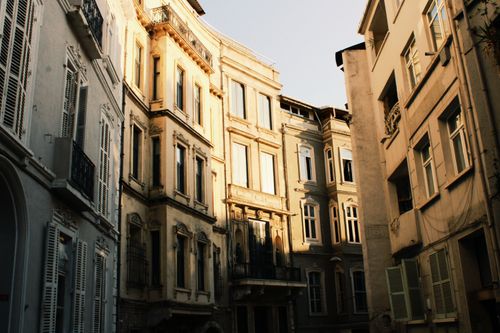 Free Sunlit historical apartment buildings with ornate details and window shutters create an architectural charm. Stock Photo