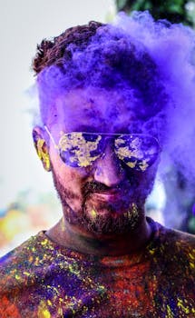 Vibrant portrait of a man celebrating Holi with colorful powder and sunglasses outdoors.
