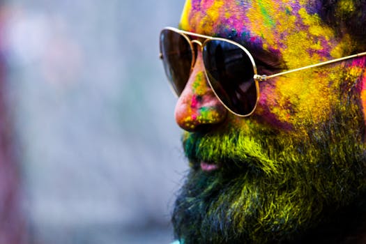 Vibrant close-up of a man with sunglasses covered in Holi festival colors.