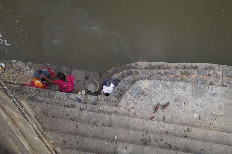 High Angle Shot Of A Person Washing Clothes On Body Of Water 