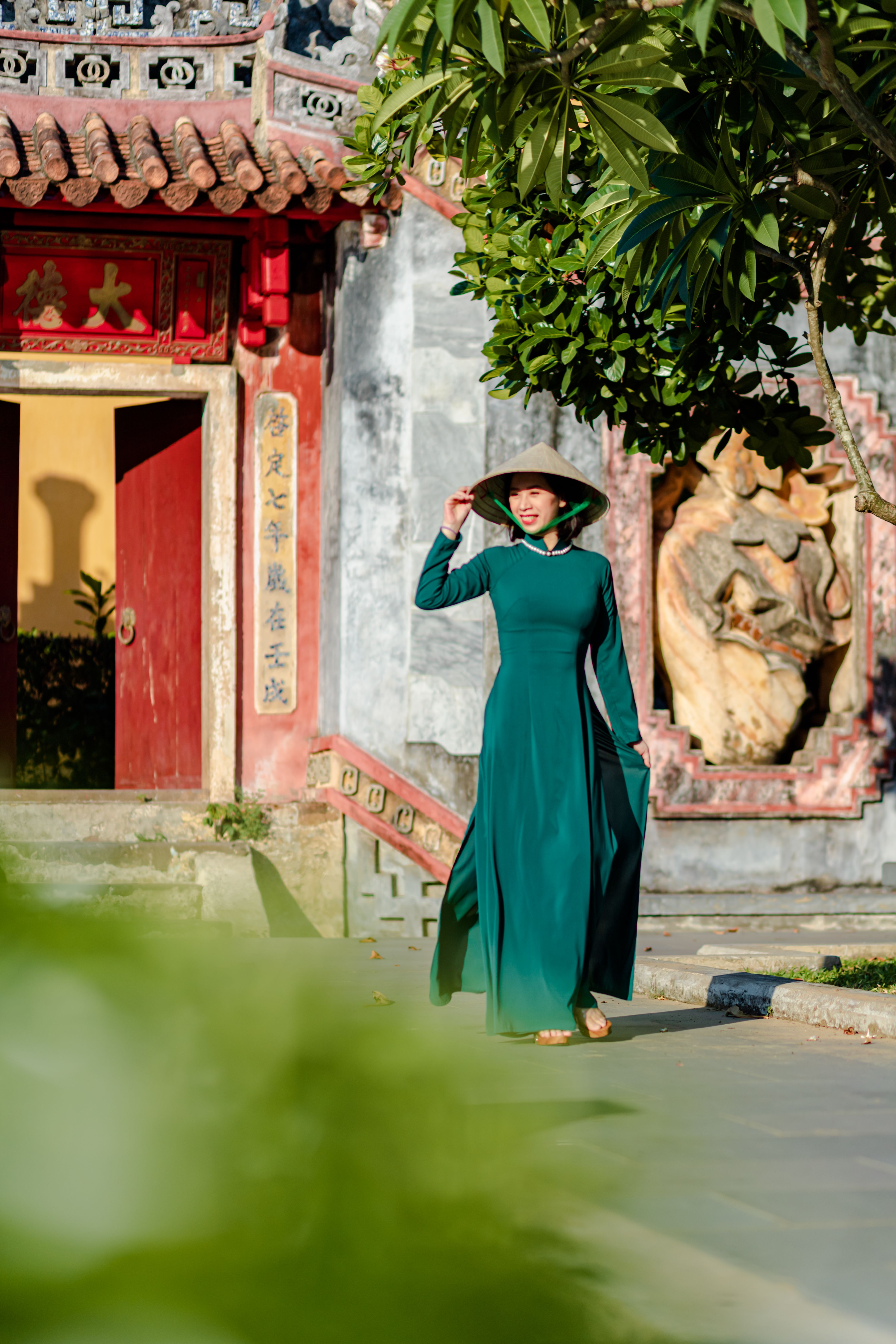 Woman in green ao dai walking past traditional Vietnamese architecture in Hoi An.