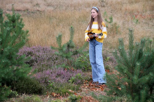 A Young Girl Standing on a Grass while Playing Ukulele