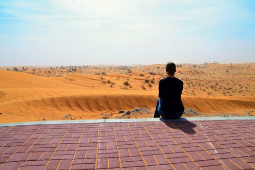 A woman sits on a ledge overlooking the scenic Ras Al-Khaimah desert dunes in daylight.