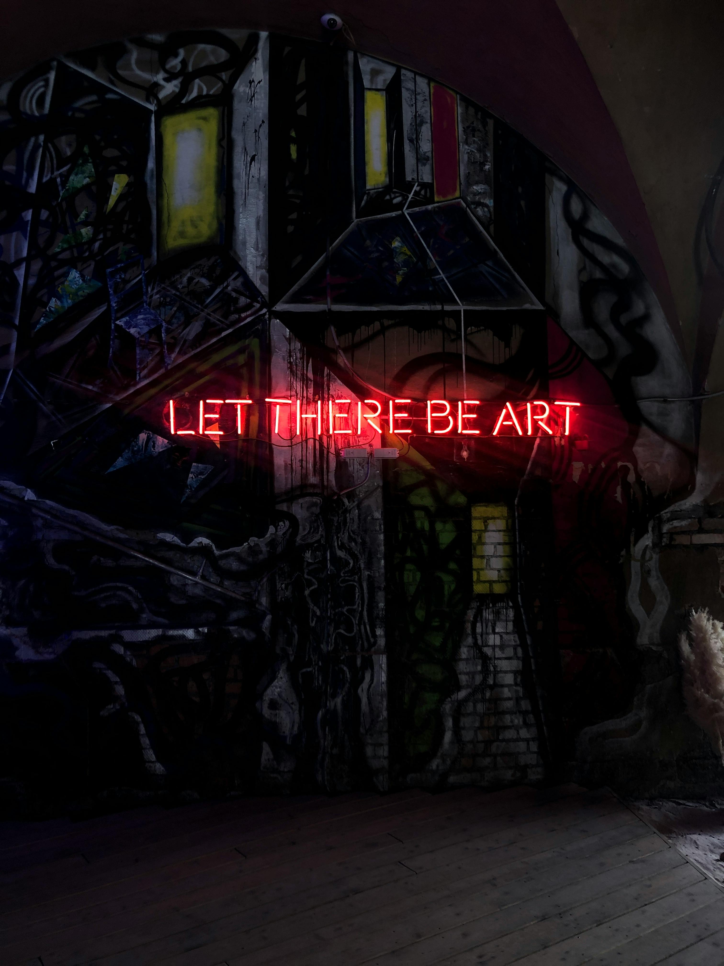 Red neon sign saying 'Let There Be Art' on artistic wall in St. Petersburg.
