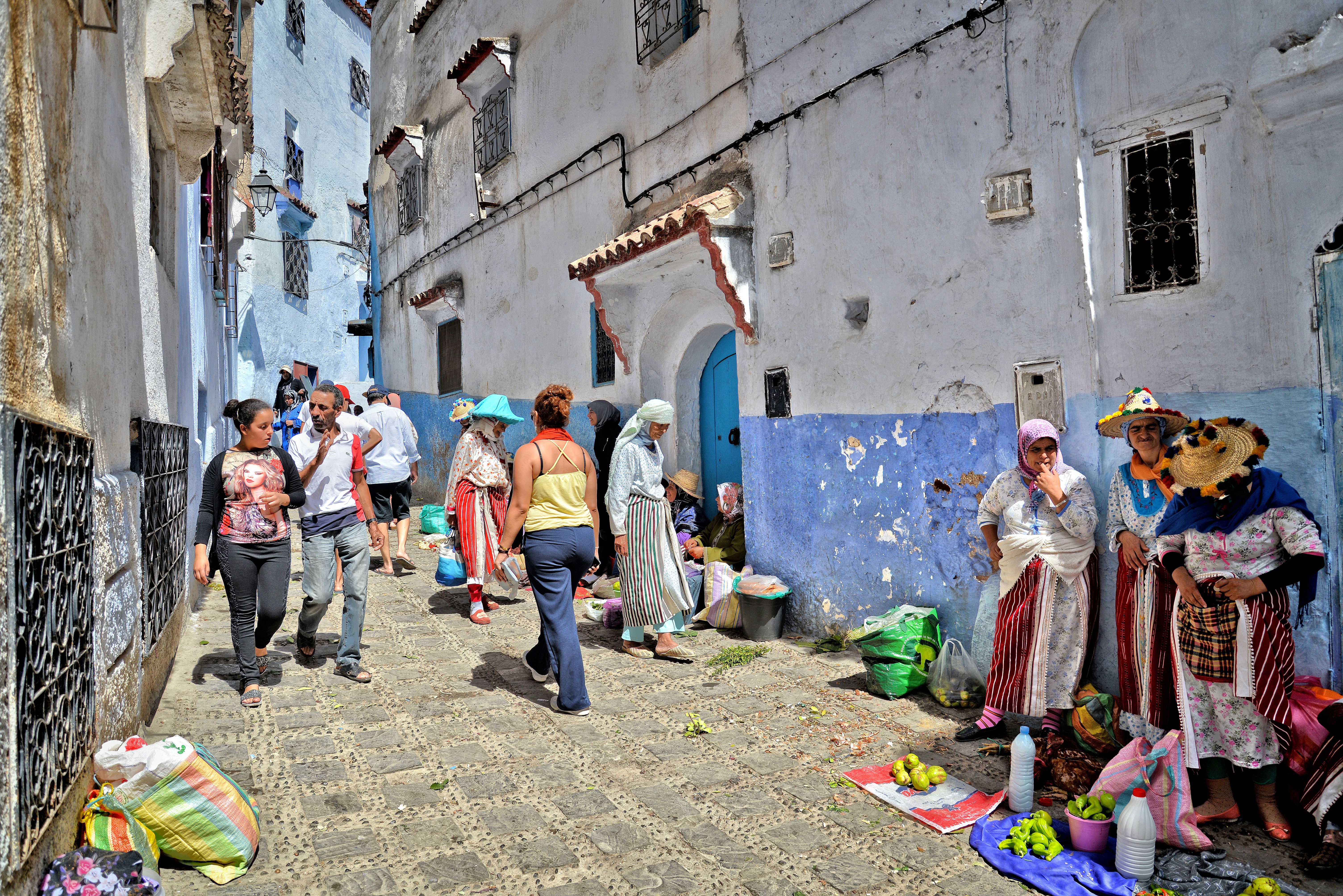 Lively street market in Chefchaouen with vendors and pedestrians in a colorful alleyway.