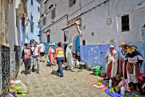 Free Lively street market in Chefchaouen with vendors and pedestrians in a colorful alleyway. Stock Photo