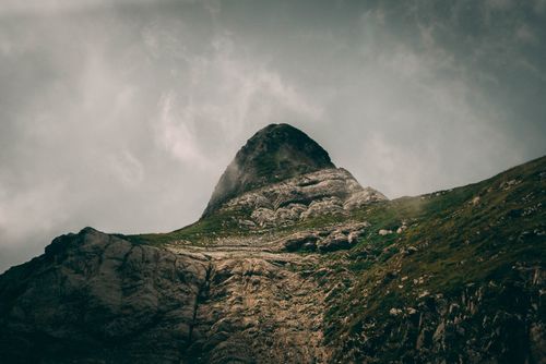 Free A striking view of a rugged mountain peak rising into a cloudy sky, showcasing nature's grandeur. Stock Photo