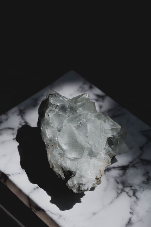 Free Apophyllite crystal elegantly resting on a marble surface, highlighted by natural light. Stock Photo