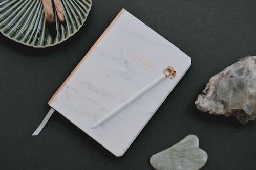 A White Notebook Beside a Crystal Stone and Gua Sha