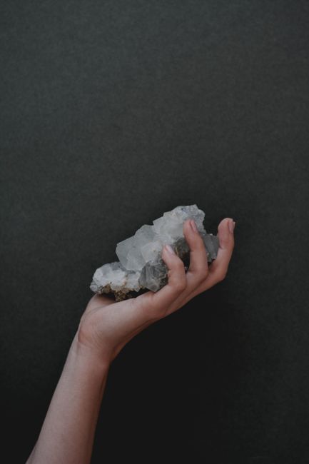 A hand gently holding a cluster of apophyllite crystals against a dark background.
