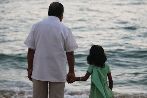 Back View Shot of Father and Daughter Holding Each Others Hands while Looking at the Sea