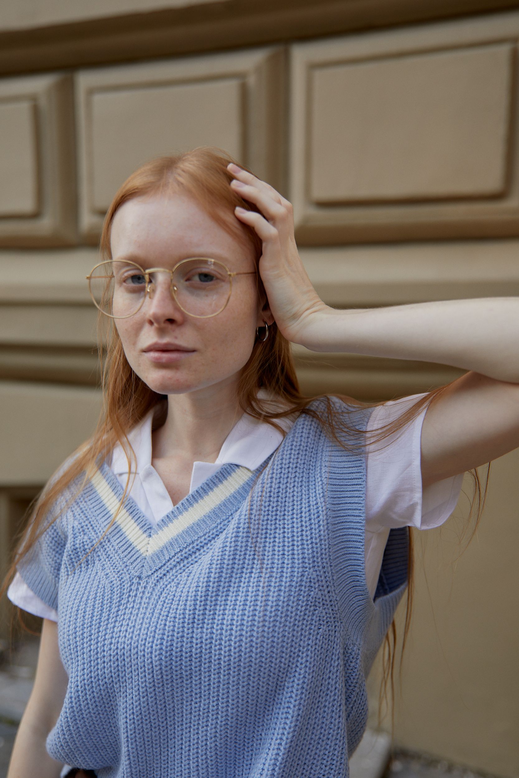 A confident young woman wearing glasses and a blue sweater vest poses outdoors.