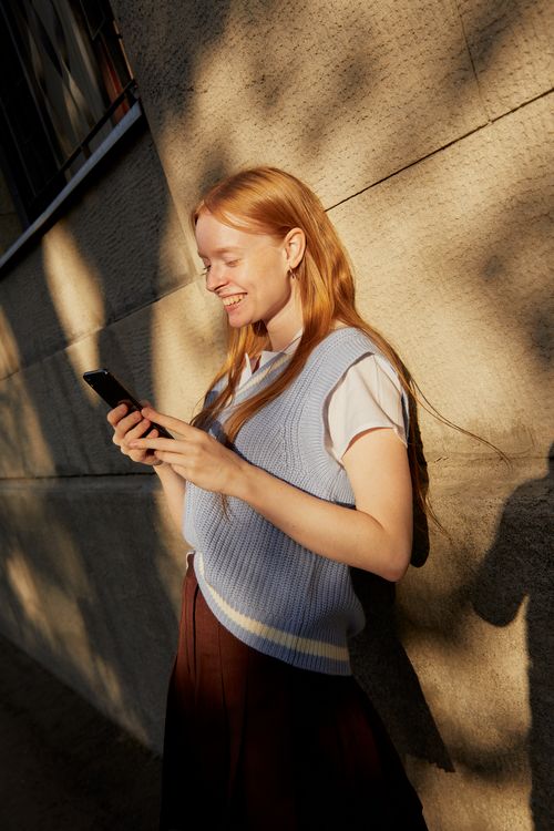 Free Smiling woman in casual fashion using a smartphone outdoors in warm lighting. Stock Photo