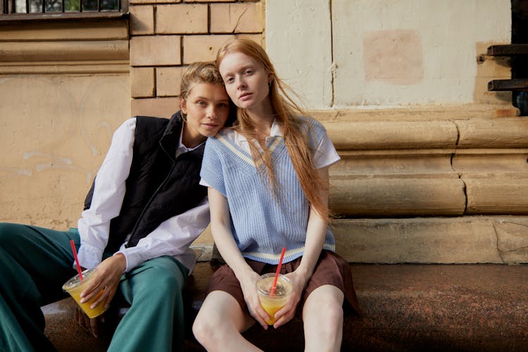 Women Sitting Together On A Concrete Stairs While Holding A Drinks