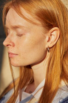 Close-up profile of a young woman with red hair and closed eyes, bathed in warm sunlight.