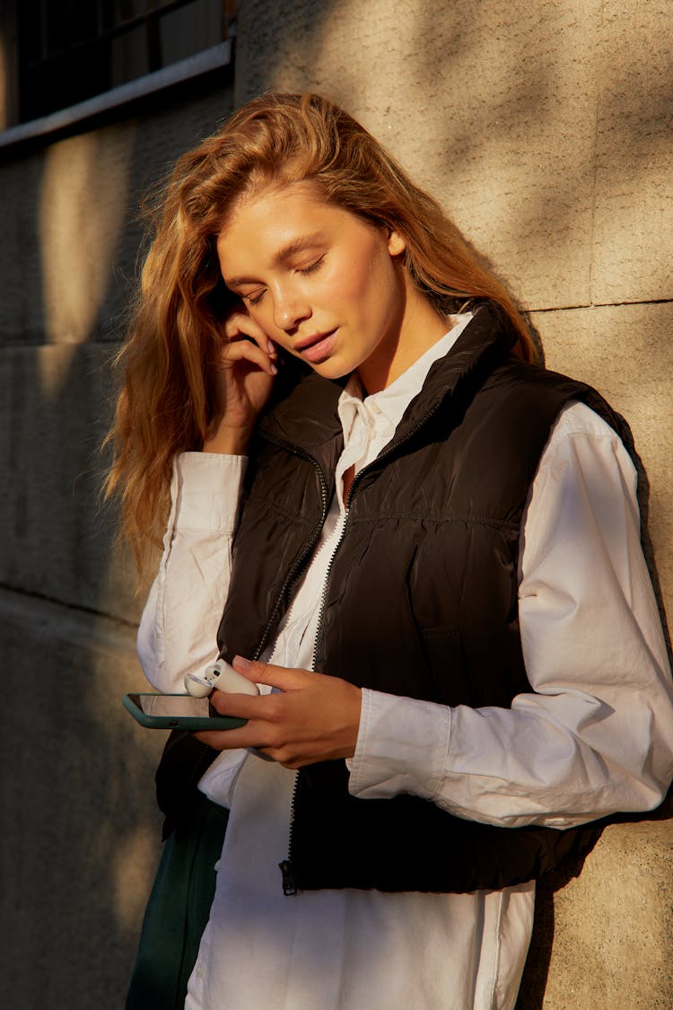 Woman In Black Vest And White Long Sleeves Holding A Phone 