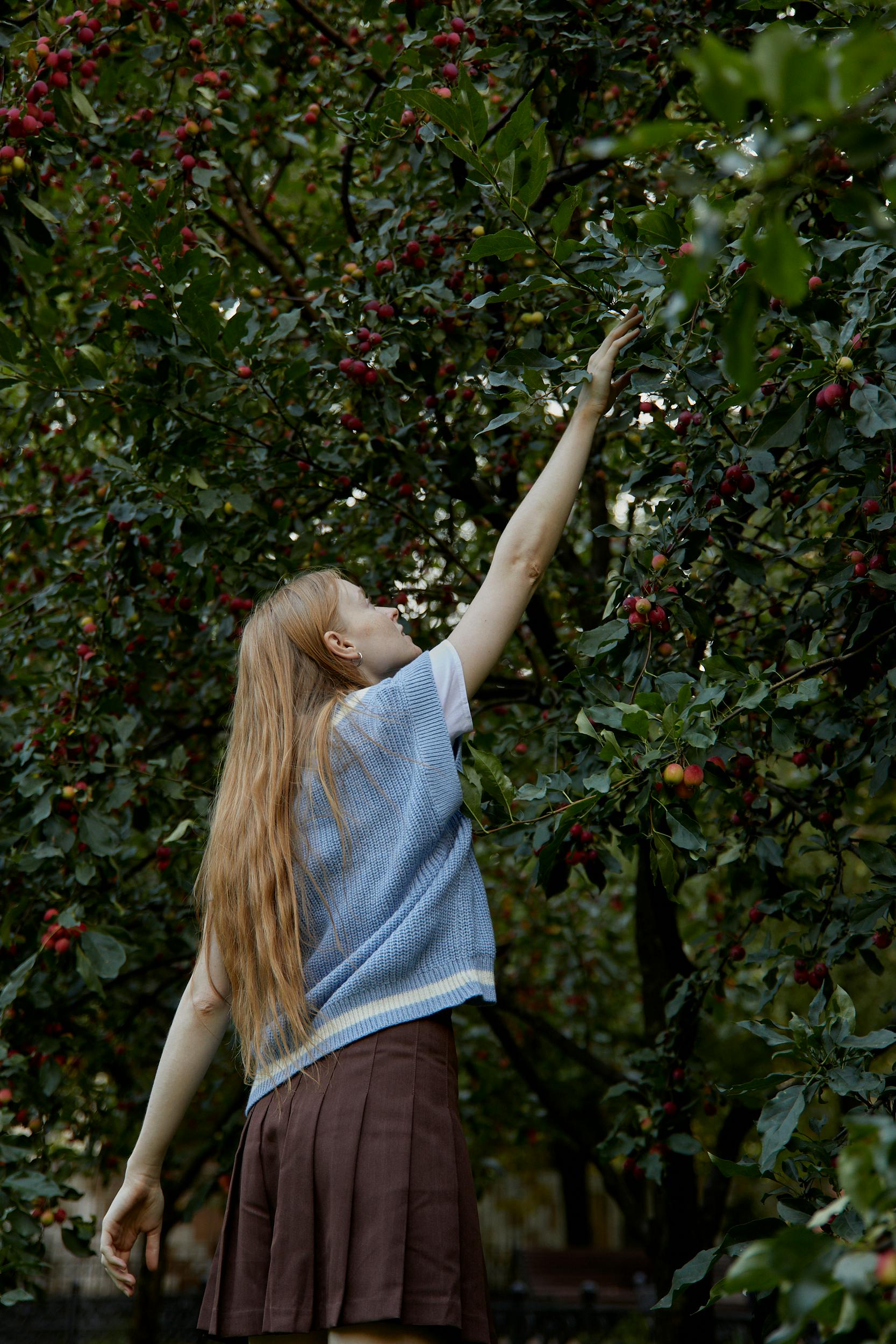 woman in brown skirt picking a red fruit