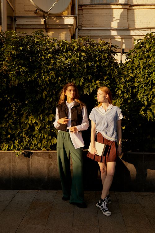 Free Two young women standing and talking casually outside in warm sunlight. Stock Photo