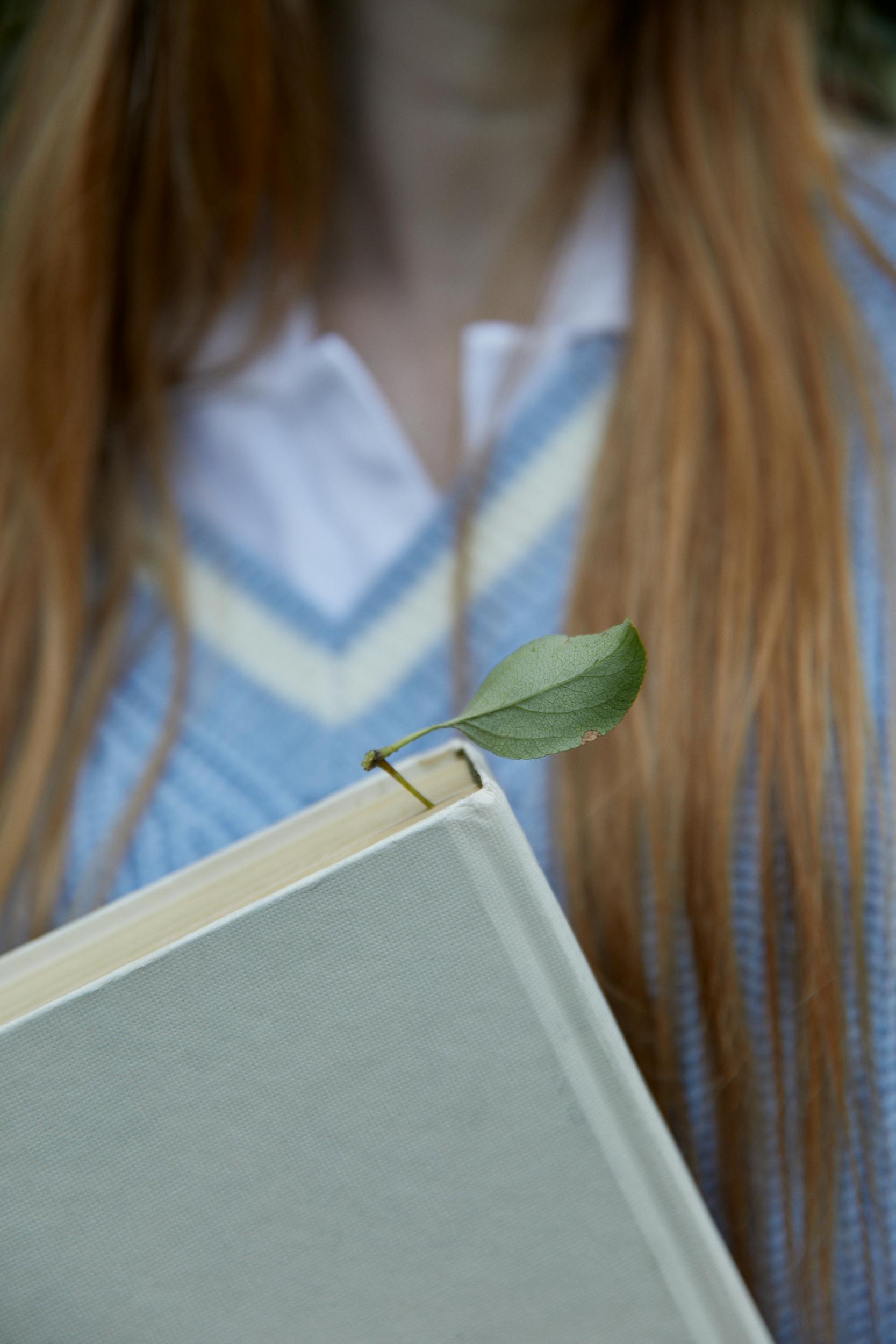Free A close-up of a book with a leaf as a bookmark, partially covering long hair. Unique and rustic composition. Stock Photo