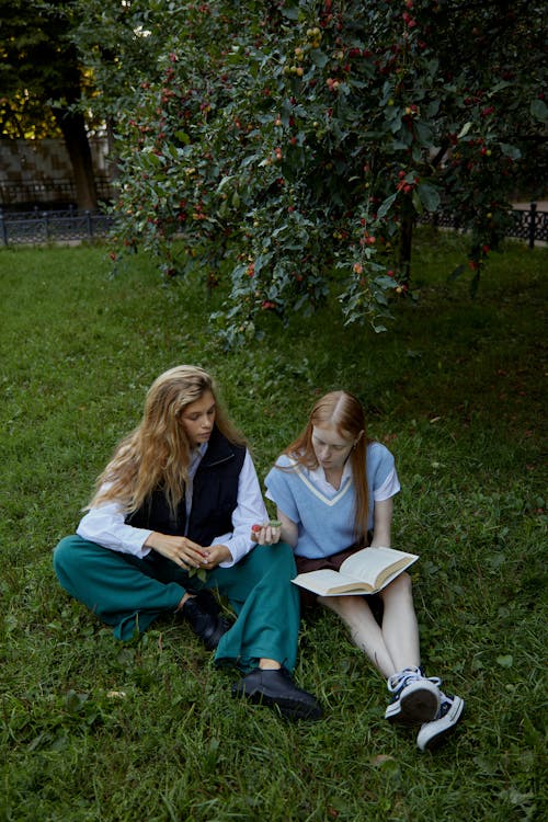 Women Sitting on Grass Field While Reading a Book 