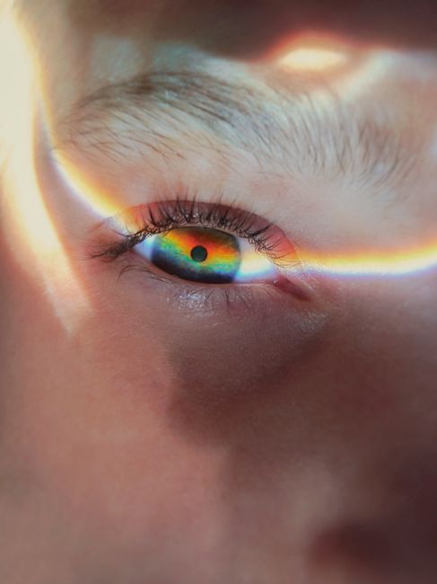 Close-up of a human eye with a captivating rainbow reflection on the iris.