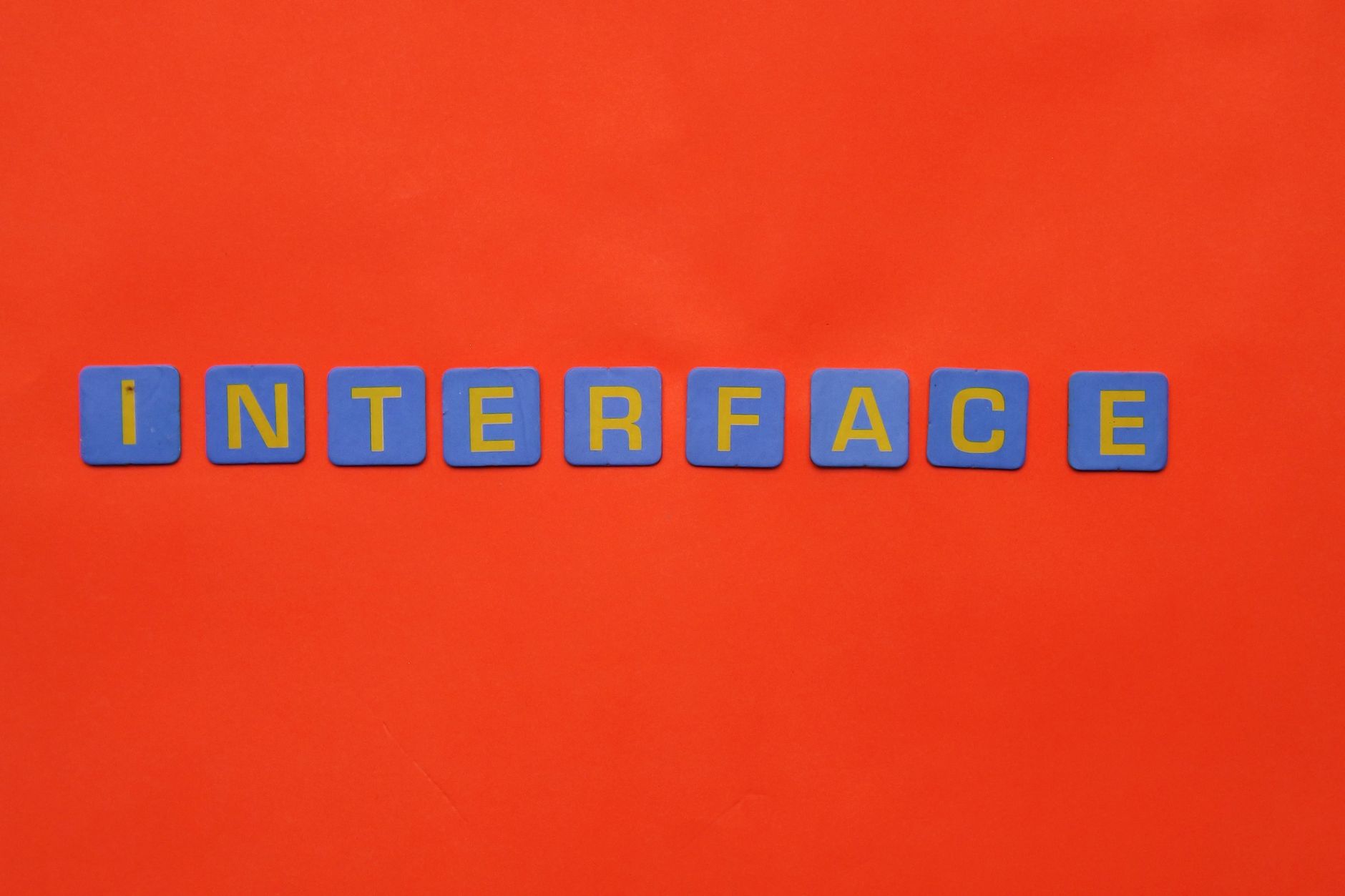 Blue blocks with yellow letters spelling 'INTERFACE' stand out against a vibrant orange backdrop.