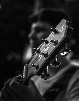 Artistic black and white photo focusing on guitar headstock with blurred musician.