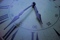 Detailed close-up of a vintage clock face with Roman numerals, focusing on the decorative hands at 30 past.