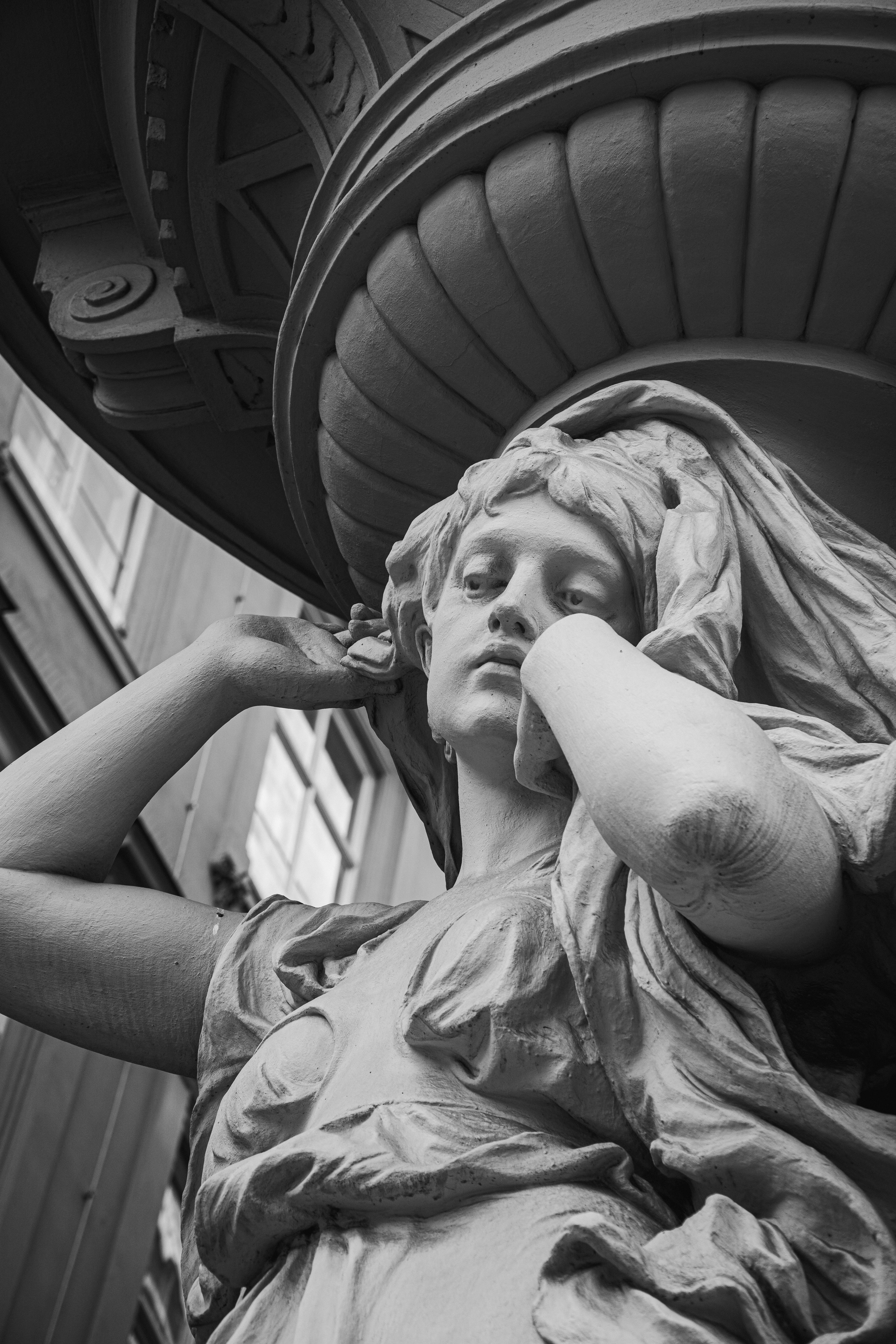 From below of black and white of sculpture of woman located in entrance of ancient building in city
