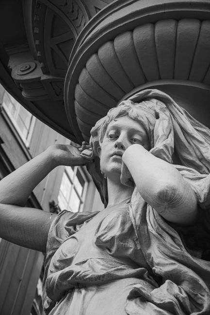 From below of black and white of sculpture of woman located in entrance of ancient building in city