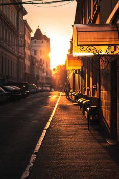 Sunset casts a warm glow on a quiet urban street lined with parked cars and buildings.