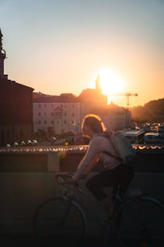 A cyclist riding across a bridge in Passau, Germany during a vibrant sunset.
