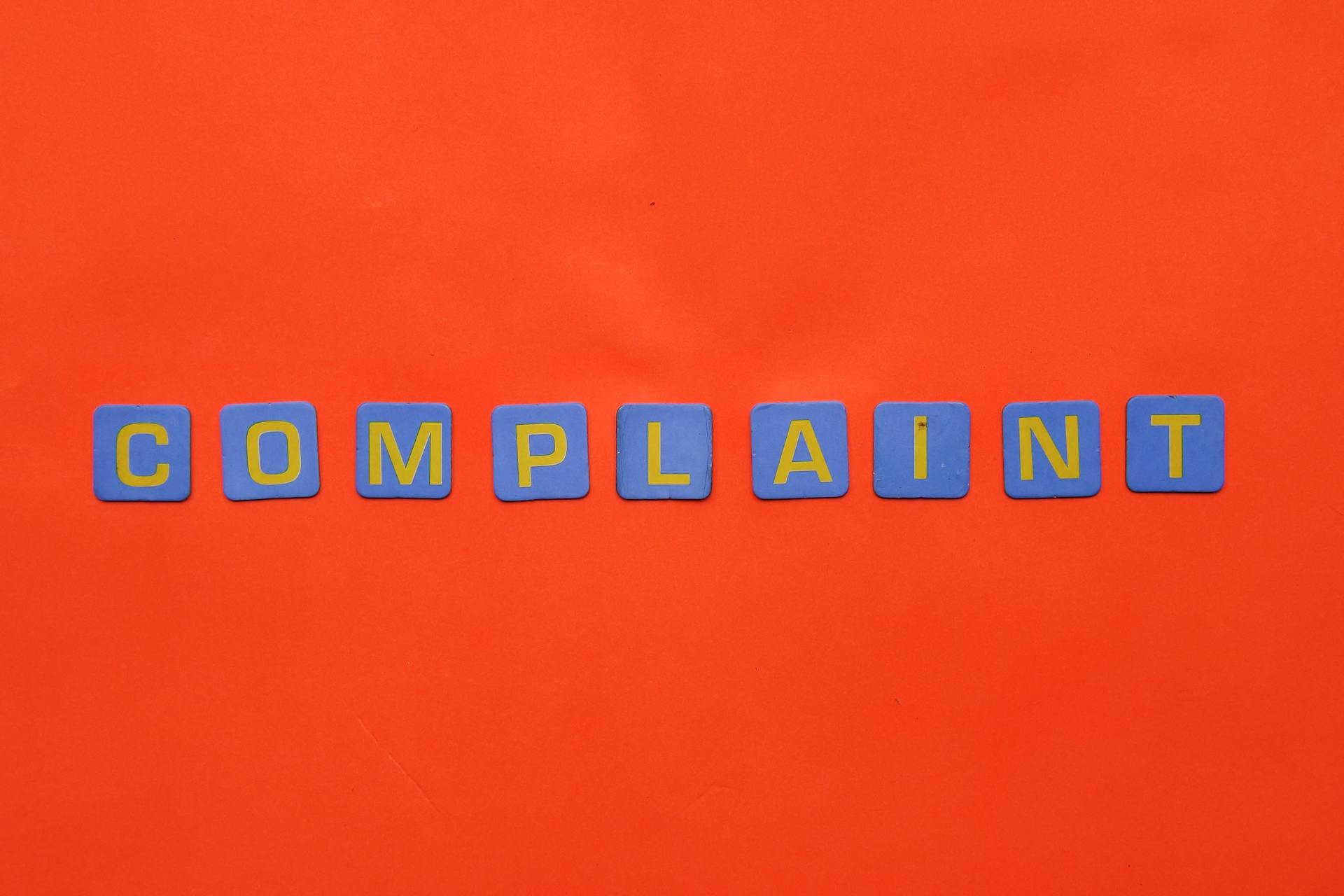 Blue letter tiles spelling 'COMPLAINT' on a vibrant red surface.