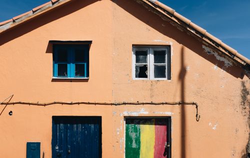 Free A run-down orange house facade with a colorful painted door and broken window under clear skies. Stock Photo