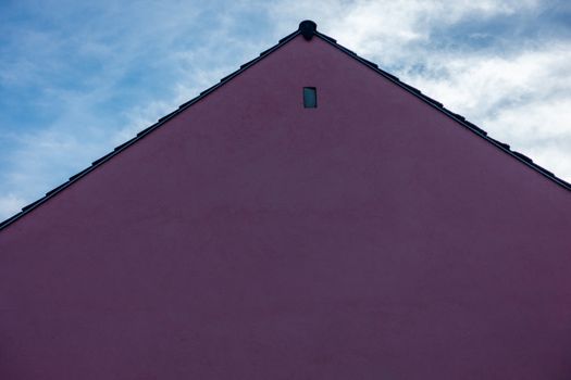 Minimalist architecture with a pink gable roof against a vibrant blue sky.