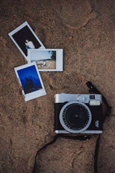 Polaroid instant camera on sand with developed photos, evoking nostalgia and travel memories.