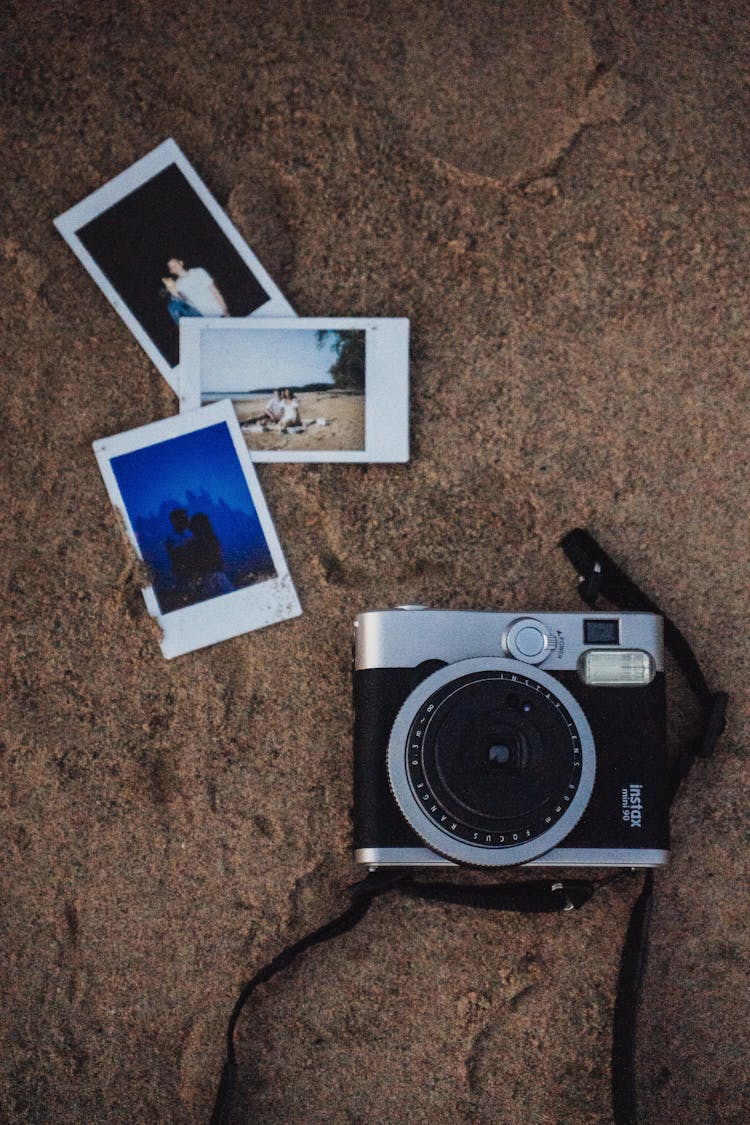 An Instax Camera And Pictures On The Sand