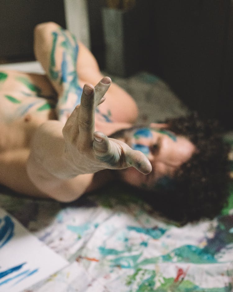 A Man Lying Down Covered In Paint Reaching His Hand Out