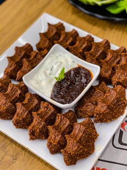 Tantalizing platter of spicy cig kofte with yogurt and red pepper dips for a flavorful snack.