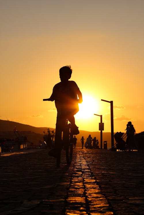 Silhouette of a Child Riding Bicycle During Sunset